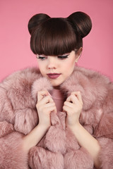 Beauty makeup. Fashion teen girl model in pink fur coat. Brunette with matte lips and bun hairstyle posing over studio background.