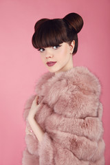 Beauty bun hairstyle.  Fashion teen girl model in pink fur coat. Brunette with matte lips makeup posing over studio background.