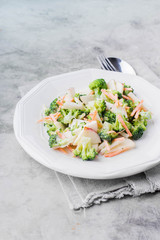 Vegetable salad with broccoli,apple,carrots, pine nuts and sauce in white plate on light stone table background. Healthy vegetarian food/ Copy space