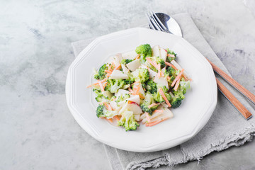 Vegetable salad with broccoli,apple,carrots, pine nuts and sauce in white plate on light stone table background. Healthy vegetarian food/ Copy space