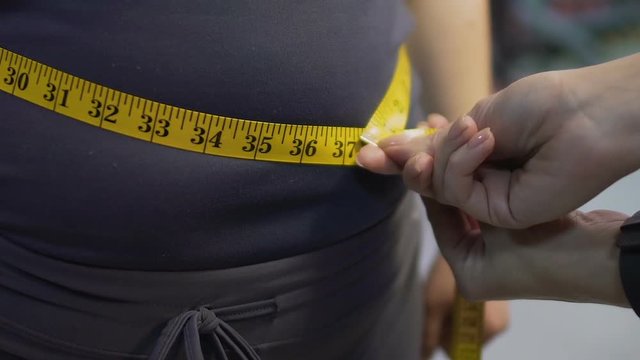 Obese female getting her waist measured with tapeline, results of weight loss
