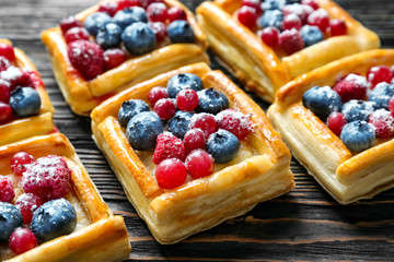 Delicious puff pastries with berries and sugar powder on wooden background