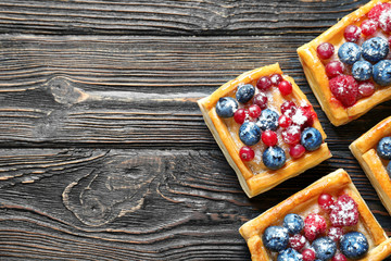 Delicious puff pastries with berries and sugar powder on wooden background