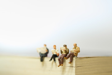 Reading and hobby concept. Group of miniature mini figures businessman, man and woman siting and...