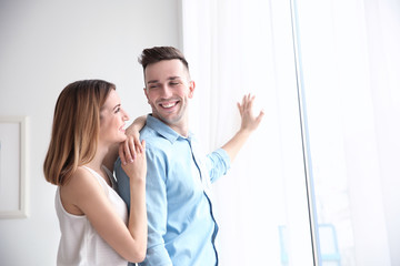Happy couple standing near window and opening curtains