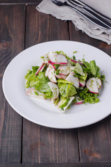 Vegetable salad with radish, cucumber, onion and lettuce in white plate on wooden table background. Healthy vegetarian food content