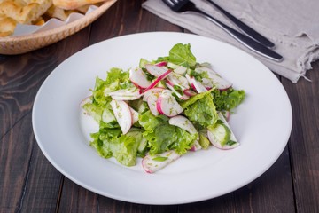 Vegetable salad with radish, cucumber, onion and lettuce in white plate on wooden table background. Healthy vegetarian food content