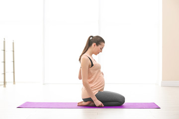 Fototapeta premium Beautiful pregnant woman doing exercise indoors