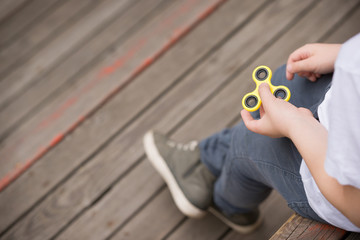 Kid boy sitting on wooden playground and playing with fidget spinner gadget - summer trend of 2017....