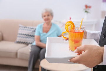 Young man serving glass of juice for elderly woman. Concept of nursing