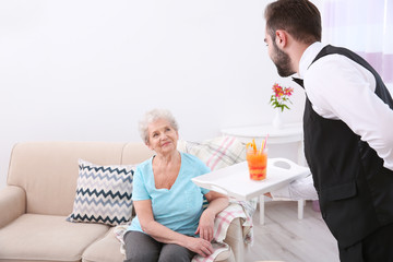 Fototapeta na wymiar Young man serving glass of juice for elderly woman. Concept of nursing