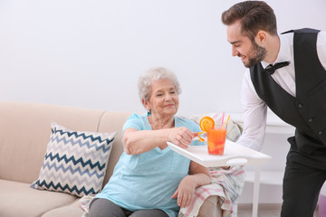Young man serving glass of juice for elderly woman. Concept of nursing