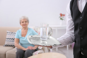 Young man serving glass of water for elderly woman. Concept of nursing