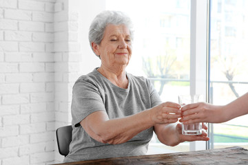 Young lady giving glass of water to elderly woman. Concept of nursing