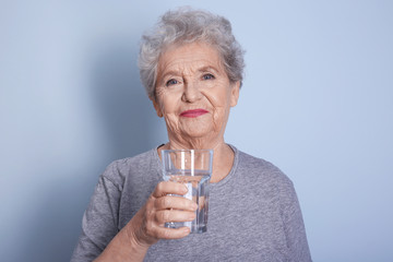 Elderly woman holding glass of water on grey background. Concept of retirement