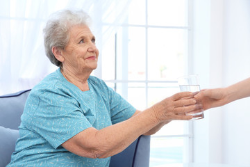 Young lady giving glass of water to elderly woman. Concept of nursing