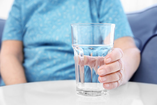 Elderly woman holding glass of water at home. Concept of retirement