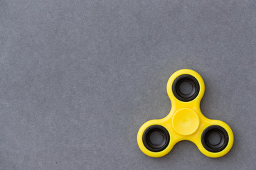 Yellow fidget spinner device on grey background. Top view. Playing with a yellow hand spinner...