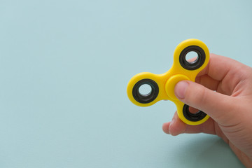 Child's hand spinning a fidget spinner device on light blue background. Top view. Playing with a...