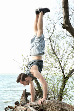 Young sporty man doing acrobatic exercises near river