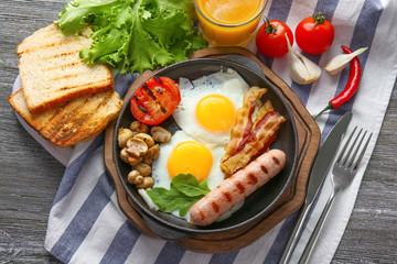 Frying pan with tasty eggs, bacon and sausage on table