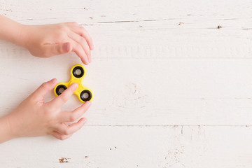 Child's hand spinning a fidget spinner device. Top view. Playing with a yellow hand spinner fidget...