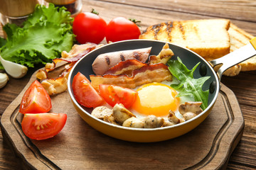 Frying pan with tasty egg, bacon and sausage on table