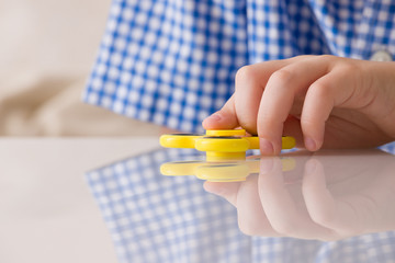 Child's hand spinning a fidget spinner device. Playing with a yellow hand spinner fidget toy