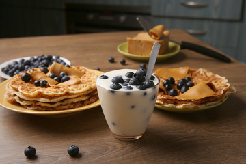 Yogurt with blueberries and heart shaped pancakes with brown caramel cheese. Sweet lunch: yogurt with blackberries and pancakes on wooden table in kitchen.
