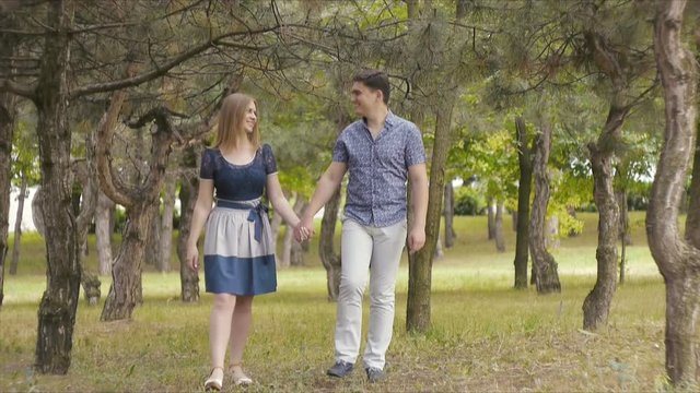 A beautiful young couple in love stroll, kiss and hug in a summer park near coniferous trees