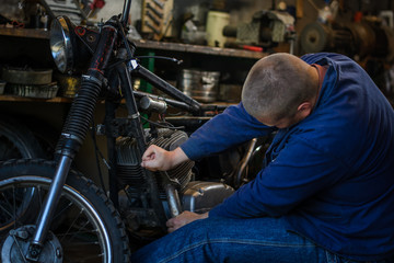 Man with tools repairing old motorcycle in workshop
