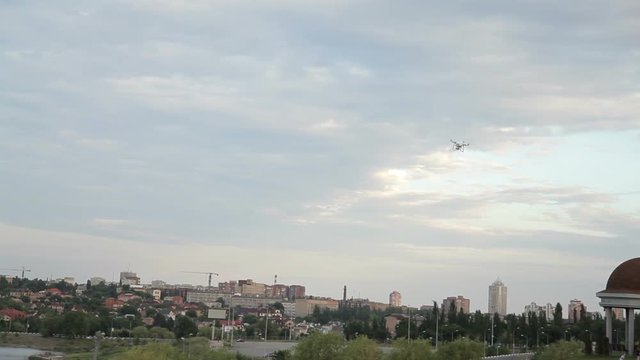 White drone quadcopter flying in the blue sky on the background of the city