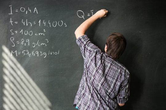 College student solving a math problem during math class in front of the blackboard/chalkboard 