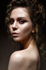 Fototapeta premium Young girl with bright evening make-up and hairdo with curls. Beautiful model with creative make-up and perfect shining skin. Beauty of the face. Photo taken in the studio.