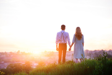 young couple is holding hands on a background sunset