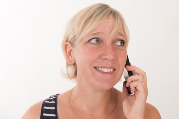 portrait of a attractive blond haired mid aged european woman wearing blue striped top acting with cellular phone - studio shot on white background.