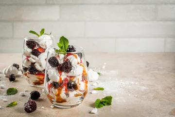  Traditional English dessert. Eton mess - whipped cream, meringue, fresh blackberries, sauce and caramel. In serving glasses on a light stone table. Copy space © ricka_kinamoto