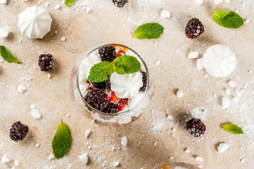 Fototapeta na wymiar Traditional English dessert. Eton mess - whipped cream, meringue, fresh blackberries, sauce and caramel. In serving glasses on a light stone table. Copy space top view