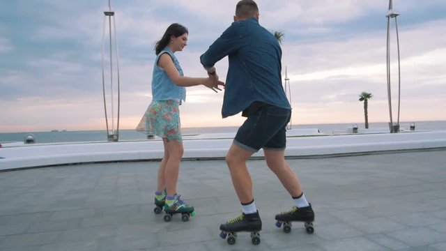 Beautiful sweet couple riding on roller skates quads holding hands near the sea, slow motion