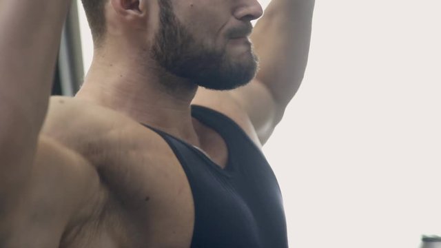 Sportsman stands and lifts weights at bottom and overhead in gym. Motion shooting of handsome brunette man in black sportswear, with bristles, with sports figure, with full biceps, flatter stomach and