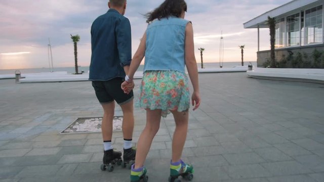 Beautiful sweet couple riding on roller skates quads holding hands near the sea