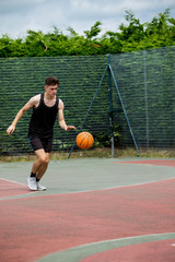Fototapeta premium Teenage boy bouncing a basketball on a court