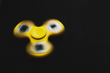 Rotating yellow fidget spinner device on black background. Top view. Playing with a yellow hand spinner fidget toy