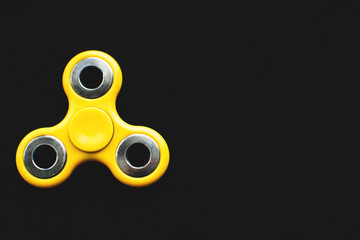 Yellow fidget spinner device on black background. Top view. Playing with a yellow hand spinner...