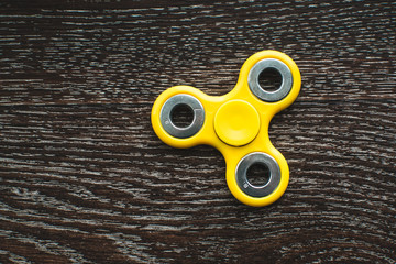 Yellow fidget spinner device on black background. Top view. Playing with a yellow hand spinner fidget toy