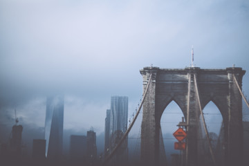 Brooklyn Bridge: tower arches & suspension cables to right of cloudy nyc skyline in background