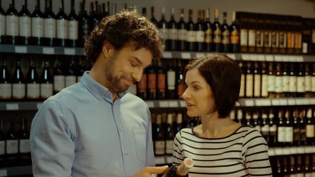 Portrait of young attractive couple choosing wine in the supermarket on background with wine bottle.