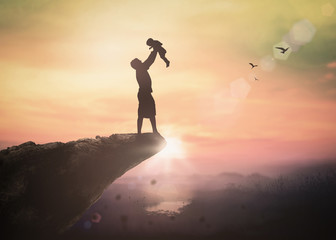Father's Day concept: Silhouette father throwing son into sky on mountain autumn sunset background. 