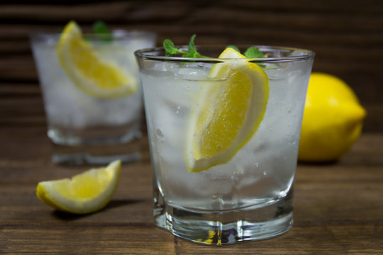 Refreshing beverage with lemon, ice and mint leaves in glasses, isolated on wooden background