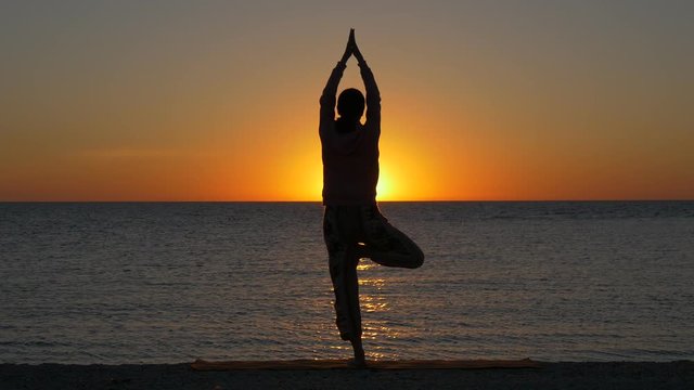 Woman in yoga pose on the beach at sunset